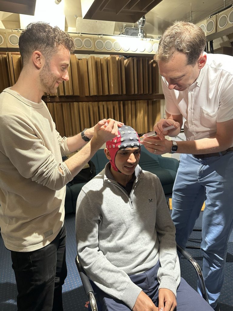 Three students setting up EEG cap with nodes. One student is seated wth the gel EEG hat on with 2 students on either side injecting gel into the EEG cap