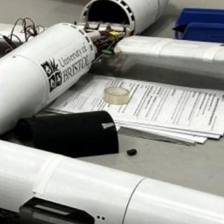 Small fixed-wing unmanned aircraft prototype on a workbench, with exposed internal components and detached fuselage section.