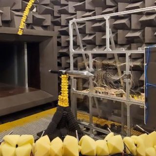 Acoustic testing chamber with sound-absorbing foam walls, measurement equipment, and cable-covered structures.