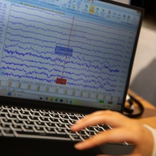 Person using a laptop displaying brainwave data and signal analysis software during neuroscience research.