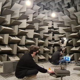 Copilot said: Researchers conducting acoustic measurements inside an anechoic chamber lined with sound-absorbing foam wedges.